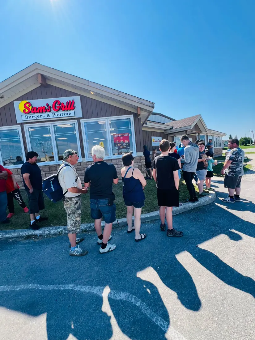 Neighbours lined up outside the Sam's Grill in Hearst, Ontario on a sunny afternoon